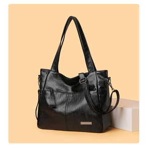 Detail of black tote bag showing pebble texture, metal logo and adjustable strap