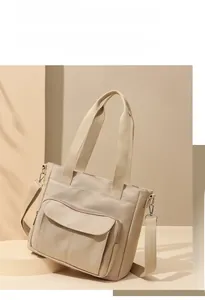 Detail of a large beige nylon tote bag with a front flap pocket on a geometric stand