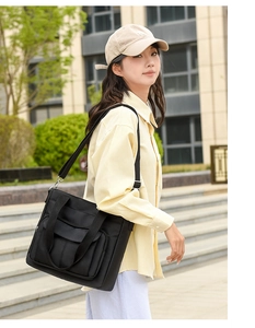 Outdoor detail of black nylon tote bag with front flap pocket and adjustable strap
