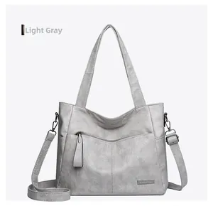 Close-up of light grey tote bag showing textured litchi grain and metallic logo detail