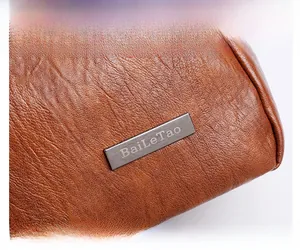 Detail of premium brown leather texture with engraved metal logo plaque and stitching