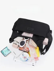 Vue de dessus d'un grand sac bandoulière en nylon noir avec divers objets de rangement