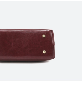 Close-up of wine red leather handbag base featuring golden protective metal feet and stitching