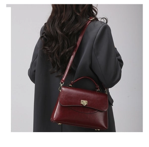 Detail of a dark red vintage leather handbag with a gold twist lock on a grey blazer