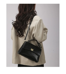Rear view of a model wearing a black minimalist PU leather crossbody bag over a beige blazer