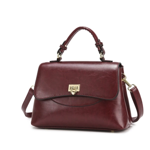 Retro burgundy leather handbag with golden trapezoid lock and detachable strap on white background