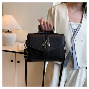Detail of black square handbag with leather texture, silver metal buckle, and zipper decoration