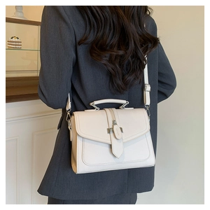 Detailed view of creamy white leather crossbody bag with silver buckle on a gray suit