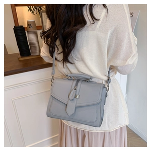 Detail of grey leather crossbody bag showing top handle and adjustable shoulder strap