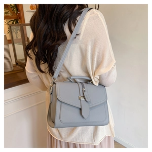 Detail of light gray square crossbody bag with silver clasp and pebble leather texture