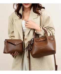 Close-up of brown leather tote and envelope bag with metal turn-lock on a beige blazer