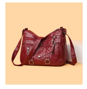 Detail of burgundy leather crossbody bag featuring multiple functional zipper pockets