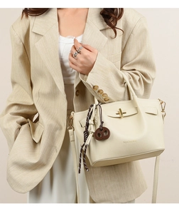 Detail of cream faux leather handbag with golden lock and fashion lettering on taupe suit