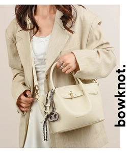 Detail of cream faux leather tote with golden twist lock and unique pretzel charm