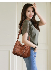 Detail of a brown leather crossbody bag featuring multiple zipper pockets and soft texture
