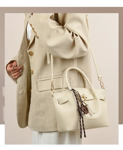 Detail of cream PU leather handbag with gold hardware and woven knot charm on shoulder strap