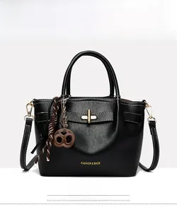 Close-up of black faux leather handbag with gold buckle and creative cookie pendant charm