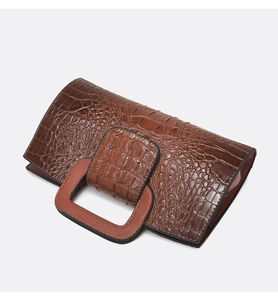 Detail der Kroko-Lederprägung an brauner Handtasche mit orangefarbenem Griff
