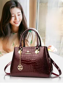 Detail of burgundy crocodile-embossed patent leather handbag with gold kangaroo emblem