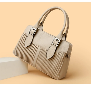 Macro detail of beige leather handbag featuring vertical pleats and silver metal hardware