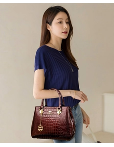 Detail of burgundy crocodile-pattern patent leather handbag with gold kangaroo emblem