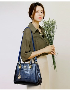 Detail of dark blue crocodile embossed tote bag with gold logo and shoulder strap