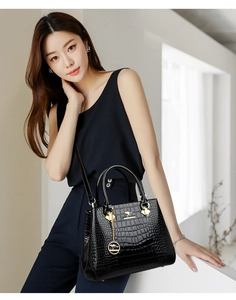 Detail of black glossy crocodile pattern handbag featuring a gold kangaroo logo and chain