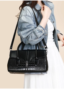 Détail d'un sac à main en cuir verni noir avec motif crocodile porté par un modèle