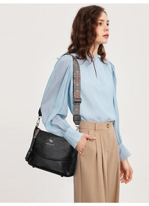 Detail einer schwarzen Leder-Eimertasche mit bunt gewebtem Schultergurt am Model