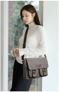 Detail of dark grey canvas messenger bag with leather straps and front pockets on model