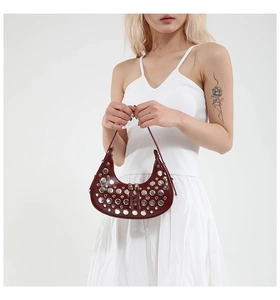 Detail of dark red crescent bucket bag featuring silver rivets and polished leather finish