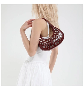 Detail of burgundy leather crescent shoulder bag featuring silver metal punk rivets