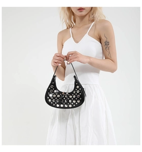 Detail of black crescent handbag featuring silver punk rivets held by a model in a white dress
