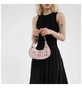 Close-up of pink crescent handbag with silver rivets worn by model in black dress