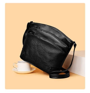 Detail of black bucket bag showing three zippered compartments and lychee leather texture