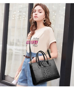 Detail of glossy crocodile embossed handbag featuring gold rivets and sturdy top handles