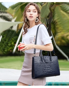 Outdoor shot of a navy blue crocodile texture handbag with shoulder strap and metal hardware