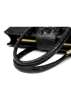 Close-up of black crocodile embossed texture with golden metal zipper and dual handles