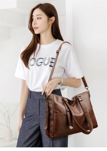 Sac fourre-tout marron foncé avec texture litchi et double sangle porté par un modèle