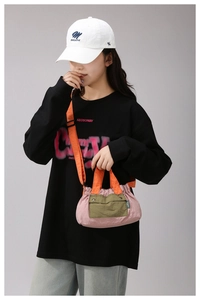 Detail of color-block nylon crossbody bag with pink body and bright orange handles
