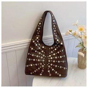 Detailaufnahme der dunkelbraunen Ledertasche mit Vintage Silbernieten auf weißem Marmor