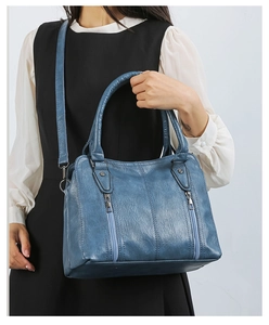 Detail of dark blue faux leather handbag featuring functional zippers and round handles