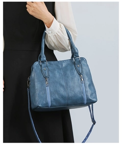 Detail of blue faux leather handbag featuring vertical zippers and dual top handles