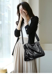 Close-up of black lychee texture leather bag with metal rivets and shoulder strap