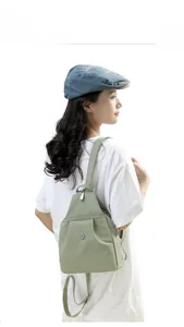 Detail view of lightweight pea green nylon backpack with silver zippers and round badge