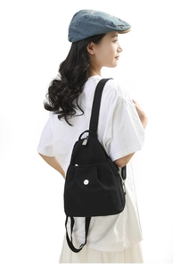 Detail view of mini black nylon backpack featuring a silver logo and front pocket
