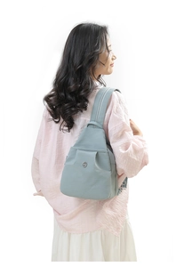 Detail view of a light blue nylon backpack with round metal logo worn by a female model