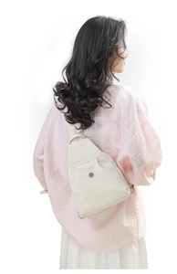 Detail of minimalist cream leather sling bag with metal logo on model's back