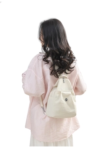 Detailed back view of a minimalist beige nylon backpack on model showing its compact size