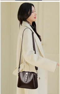 Detail of dark brown polished leather crossbody bag with metallic rotary lock on a model